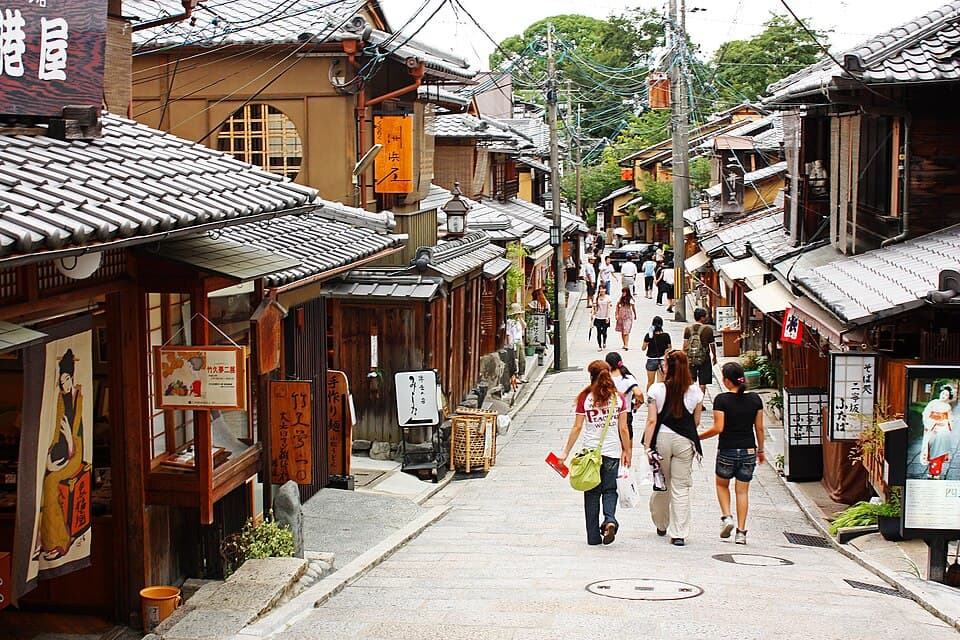 Visitors walking up Sannenzaka, a sloping lane of tiled wooden shopfronts with hanging signs.